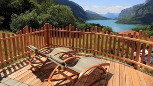 Une terrasse en bois avec deux chaises longues donnant sur un lac et des montagnes.