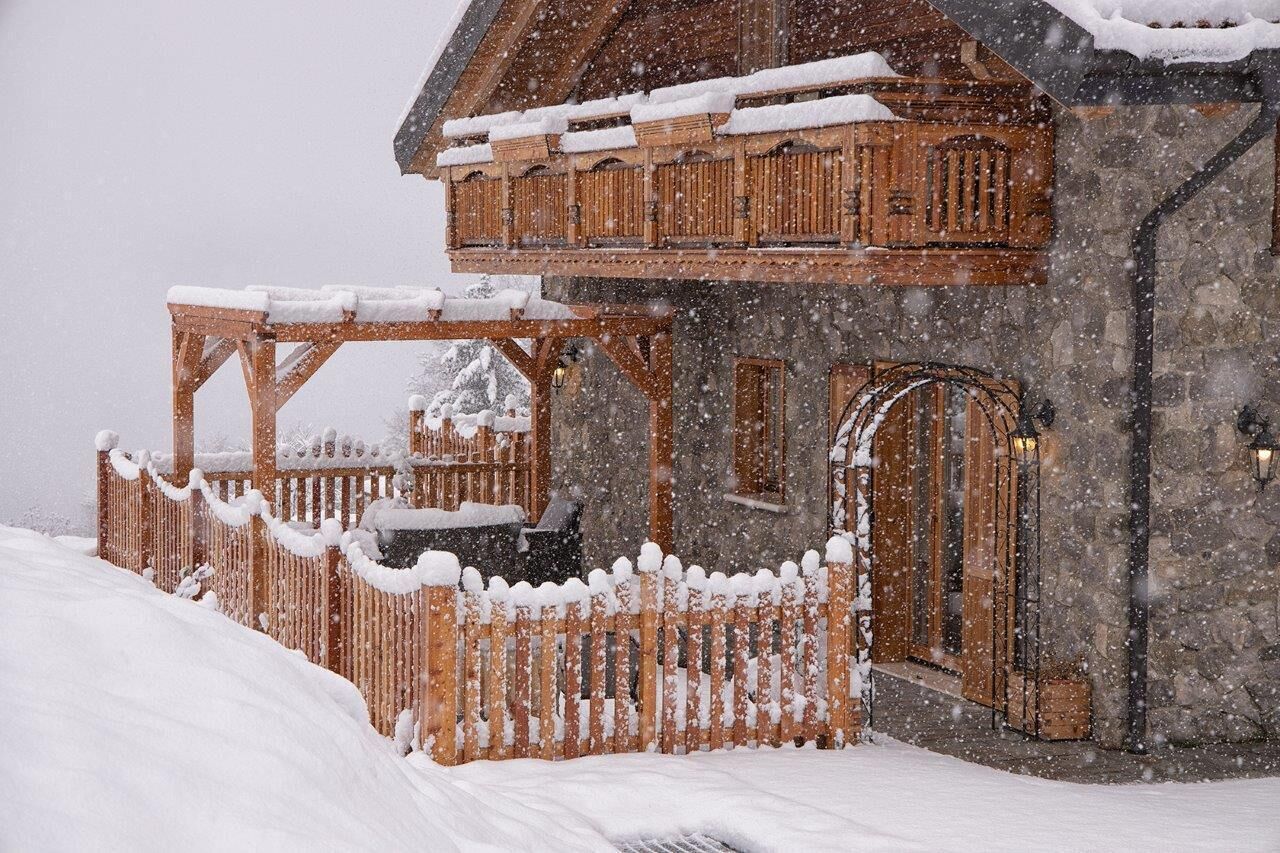 Eine Holzhütte mit Balkon und Natursteinfassade, umgeben von einem Holzzaun und Schnee.