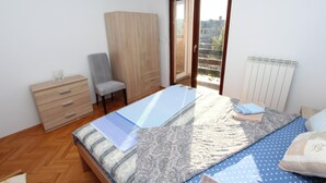A bedroom with a bed, a wooden wardrobe, a chair, a radiator, and a window with a view. - NATALI Three-Bedroom Apartment (Rovinj)