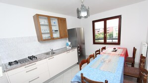 A kitchen with a dining table, wooden cabinets, and a window. - NATALI Three-Bedroom Apartment (Rovinj)