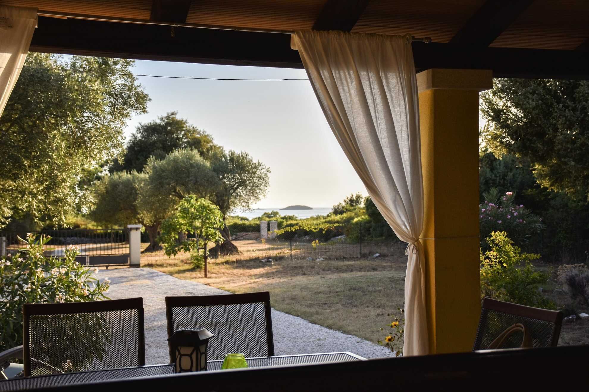 Un patio al aire libre con una mesa y sillas, con vistas a un jardín con árboles y el mar.