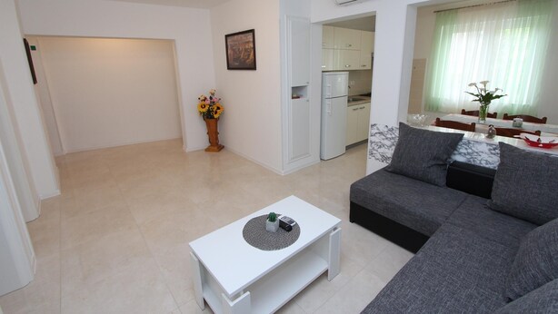 A modern living room with a grey sofa, a white coffee table, and a kitchen area visible through an open door. - PALAZIOL Two-Bedroom Apartment 1 (Rovinj)