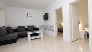 A modern living room with a grey sectional sofa, a white coffee table, and a flat-screen TV mounted on the wall. - PALAZIOL Two-Bedroom Apartment 1 (Rovinj)