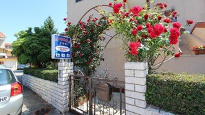 A gated entrance with a sign for AURORA APARTMENTS, a white car parked nearby, and a potted plant with red flowers.