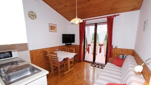 A compact room with a kitchenette, a dining area, a sofa, and a television.