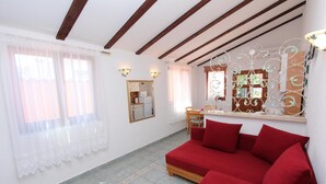 A room with a red sofa, a wooden-framed ceiling, a kitchen area, and a decorative mirror. - LUCU One-Bedroom Apartment (veći) (Rovinj)