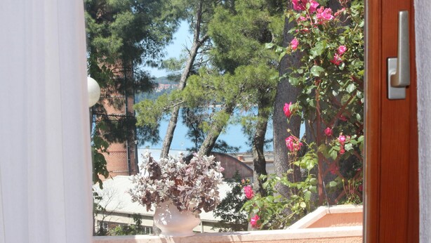A window with a view of a coastal area, a white vase with dried flowers, and a wooden door. - LUCU One-Bedroom Apartment (veći) (Rovinj)