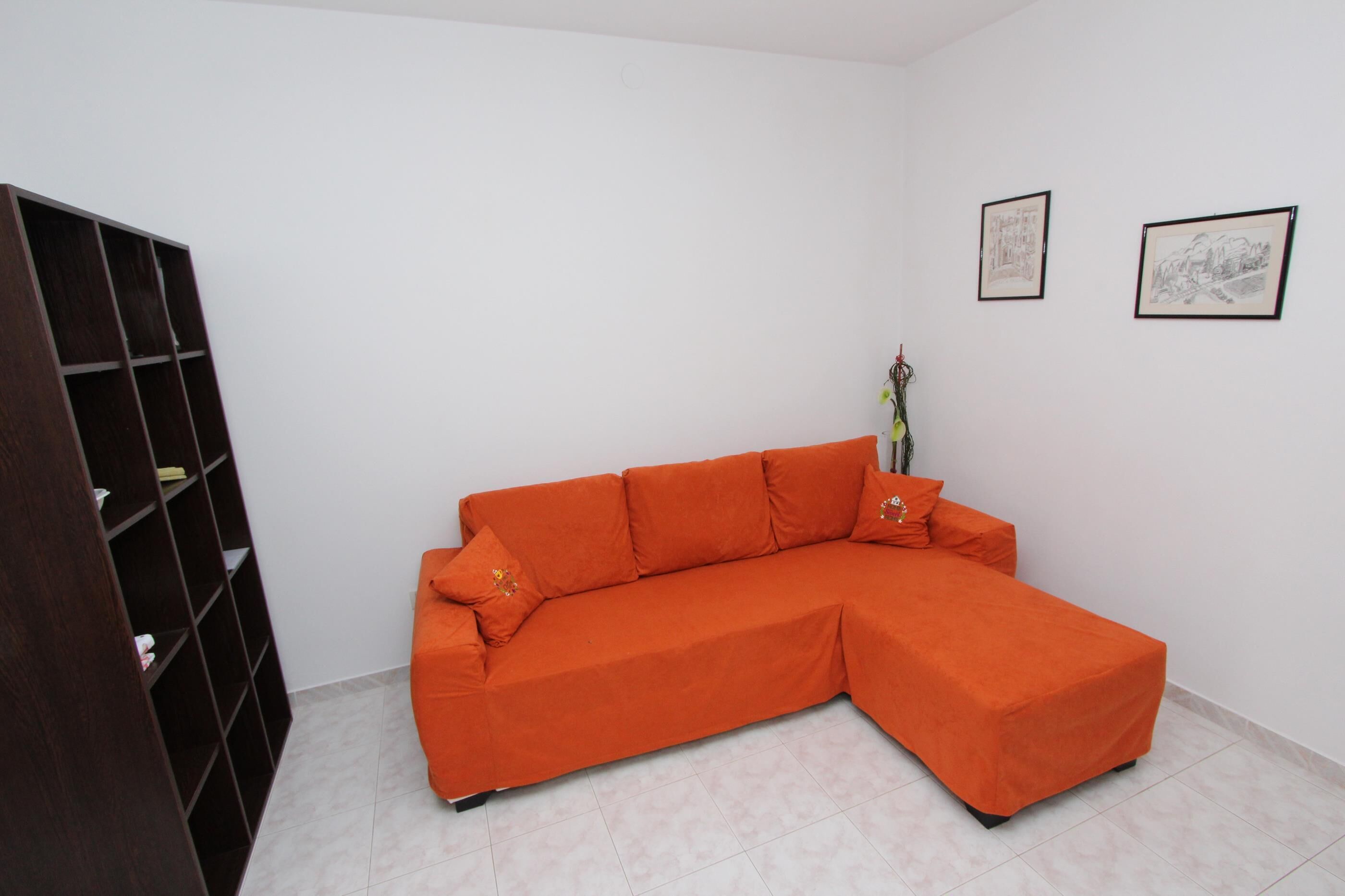 Une pièce comprenant un grand canapé d’angle orange, une bibliothèque en bois foncé et deux œuvres d’art encadrées accrochées au mur.