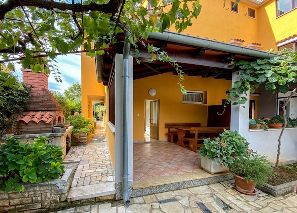 A covered outdoor patio with stone flooring, a brick chimney, and potted plants. - MALVINA #1 Two-Bedroom Apartment (Rovinj)