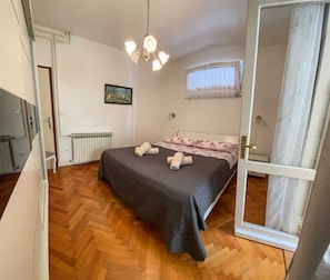 A bedroom with a bed, a radiator, a picture on the wall, and a window with curtains. - MALVINA #1 Two-Bedroom Apartment (Rovinj)