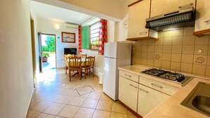 Cocina compacta con estufa a gas, refrigerador y comedor con sillas y mesa.