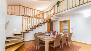 A dining area with a wooden staircase, a dining table set for four, and a view of the upper floor. - VILLA NERA Three-Bedroom Apartment (Pula)
