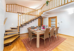 A dining area with a wooden staircase, a dining table set for four, and a view of the upper floor.