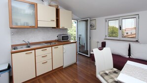 Une cuisine compacte équipée d’un four à micro-ondes, d’un évier et de placards en bois. Une porte coulissante donne accès à un balcon.