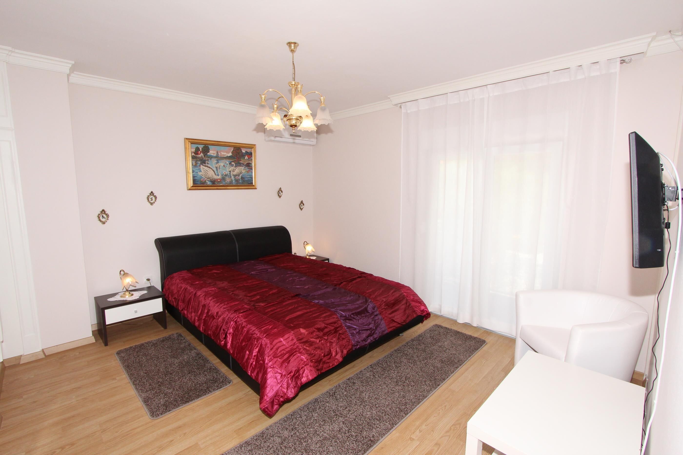 Un dormitorio con cama, mesitas de noche, escritorio, silla, televisión y un cuadro en la pared.