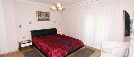 Un dormitorio con cama, mesitas de noche, escritorio, silla, televisión y un cuadro en la pared.