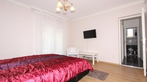 Un dormitorio con una cama grande, un televisor montado en la pared, una silla blanca y una puerta que da a un baño.