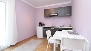 Cocina compacta con una mesa y sillas blancas, un refrigerador pequeño y una cafetera.