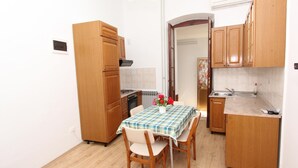 A compact kitchen with wooden cabinets, a dining table with chairs, and a radiator. - RIKI Two-Bedroom Apartment (Rovinj)