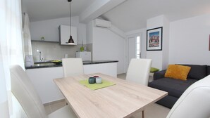 A modern living space with a dining table, chairs, a sofa, and a kitchen area. - SORRISO One-Bedroom Apartment (Rovinj)