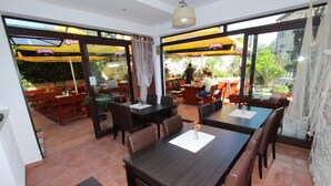 An indoor dining area with tables and chairs, large windows, and outdoor seating visible through the glass doors. - SORRISO One-Bedroom Apartment (Rovinj)