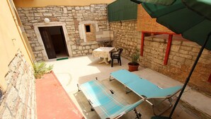 A patio with a table and chairs, a blue lounge chair, a potted plant, and a stone wall. - PUPA Studio Apartment (Rovinj)