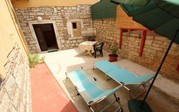 A patio with a table and chairs, a blue lounge chair, a potted plant, and a stone wall.