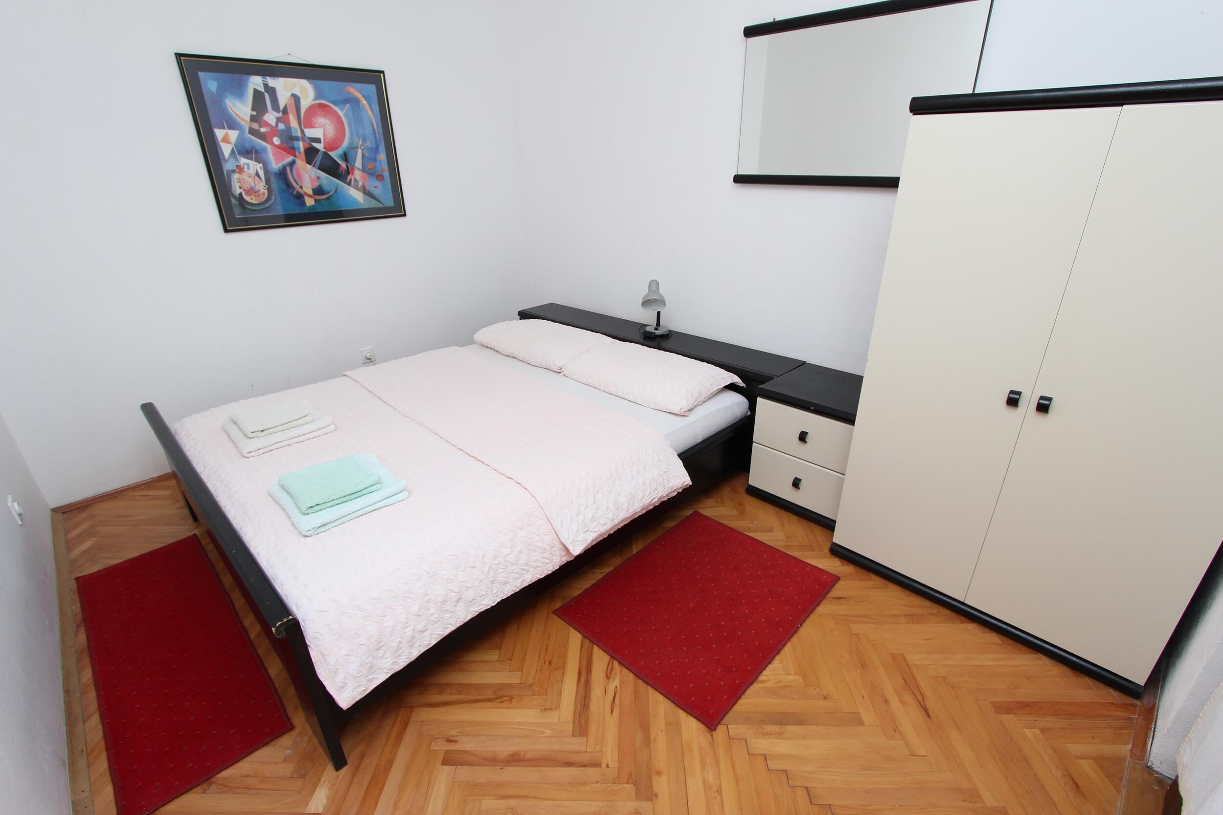 A bedroom with a bed, a nightstand, a wardrobe, and a painting on the wall.