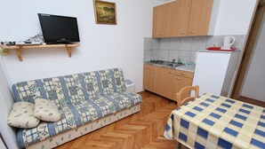 A compact living space with a sofa, a small table, a kitchenette, and a TV on a shelf. - LORA One-Bedroom Apartment 3 (Rovinj)