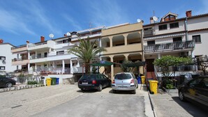 A residential building with multiple balconies, a parking area, and a palm tree. - LORA One-Bedroom Apartment 3 (Rovinj)