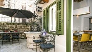 Eine Terrasse im Freien mit Steinböden, Metallstühlen, einem Tisch mit einer violetten Vase und einem großen Sonnenschirm.