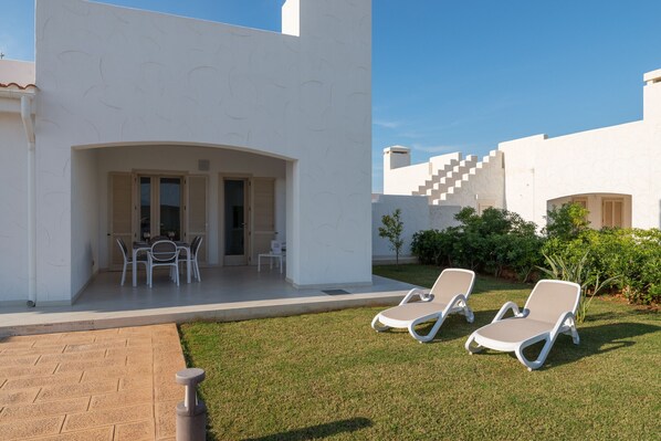 A modern outdoor area with a patio, two lounge chairs, a table with chairs, and a small garden. - Blue Sea Villa Maestrale by Wonderful Italy (Ostuni)