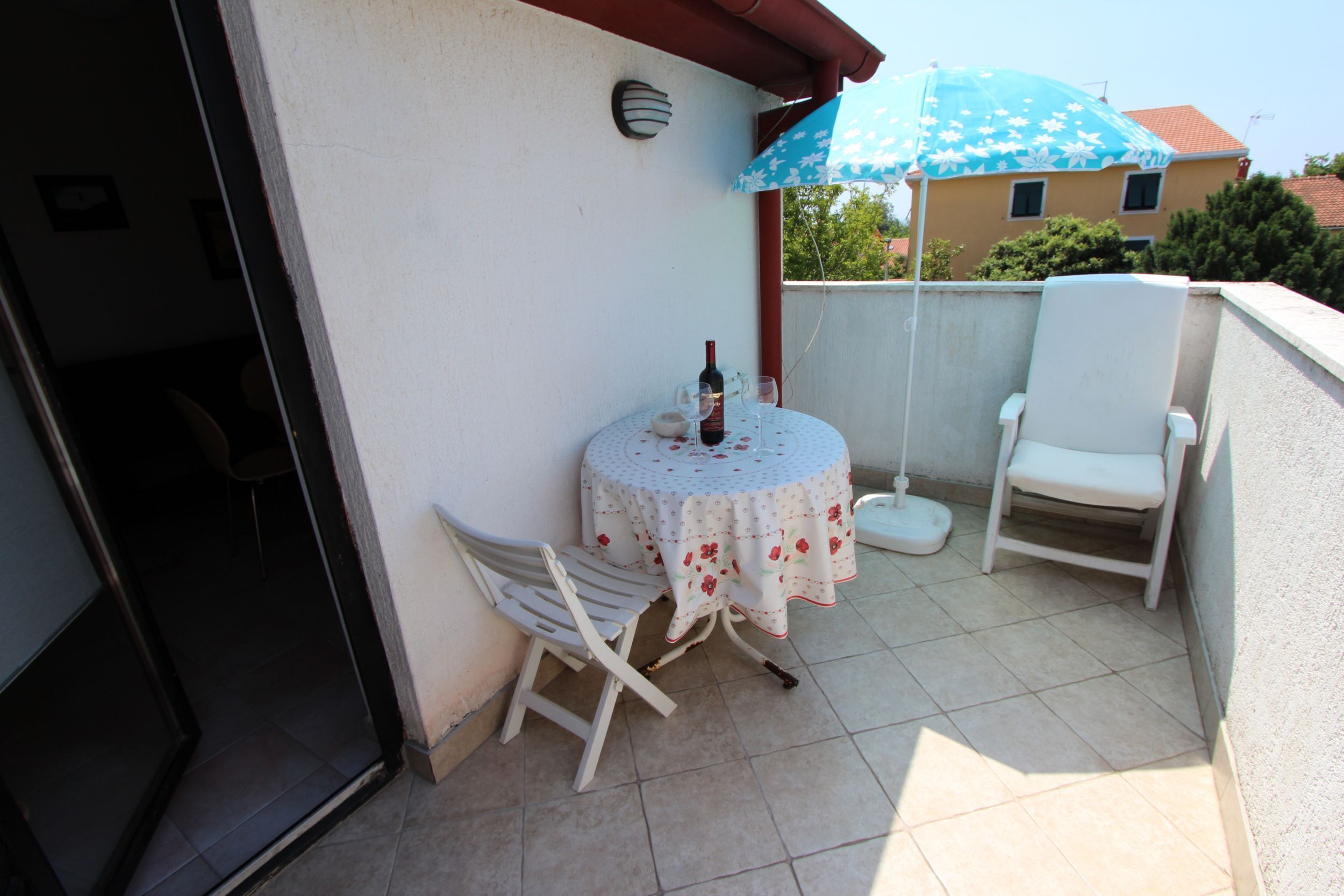 Un petit balcon avec une table, des chaises, une bouteille et un parasol bleu.