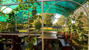 A covered outdoor seating area with benches and tables, surrounded by greenery and a fence. - VILLA FJORD Two-Bedroom Apartment 2 (Kanfanar)