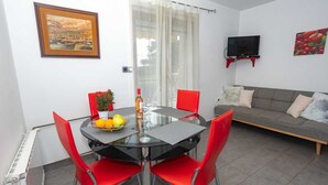 A modern living room with a glass dining table, red chairs, a sofa, and a TV mounted on the wall. - VILLA FJORD Two-Bedroom Apartment 2 (Kanfanar)