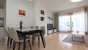 A modern living room with a dining area, a TV, and a large window with curtains.
