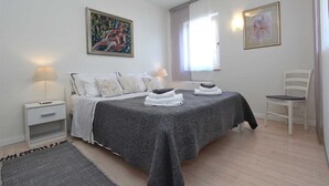 A bedroom with a bed, two bedside tables, a chair, a rug, and two paintings on the walls.
