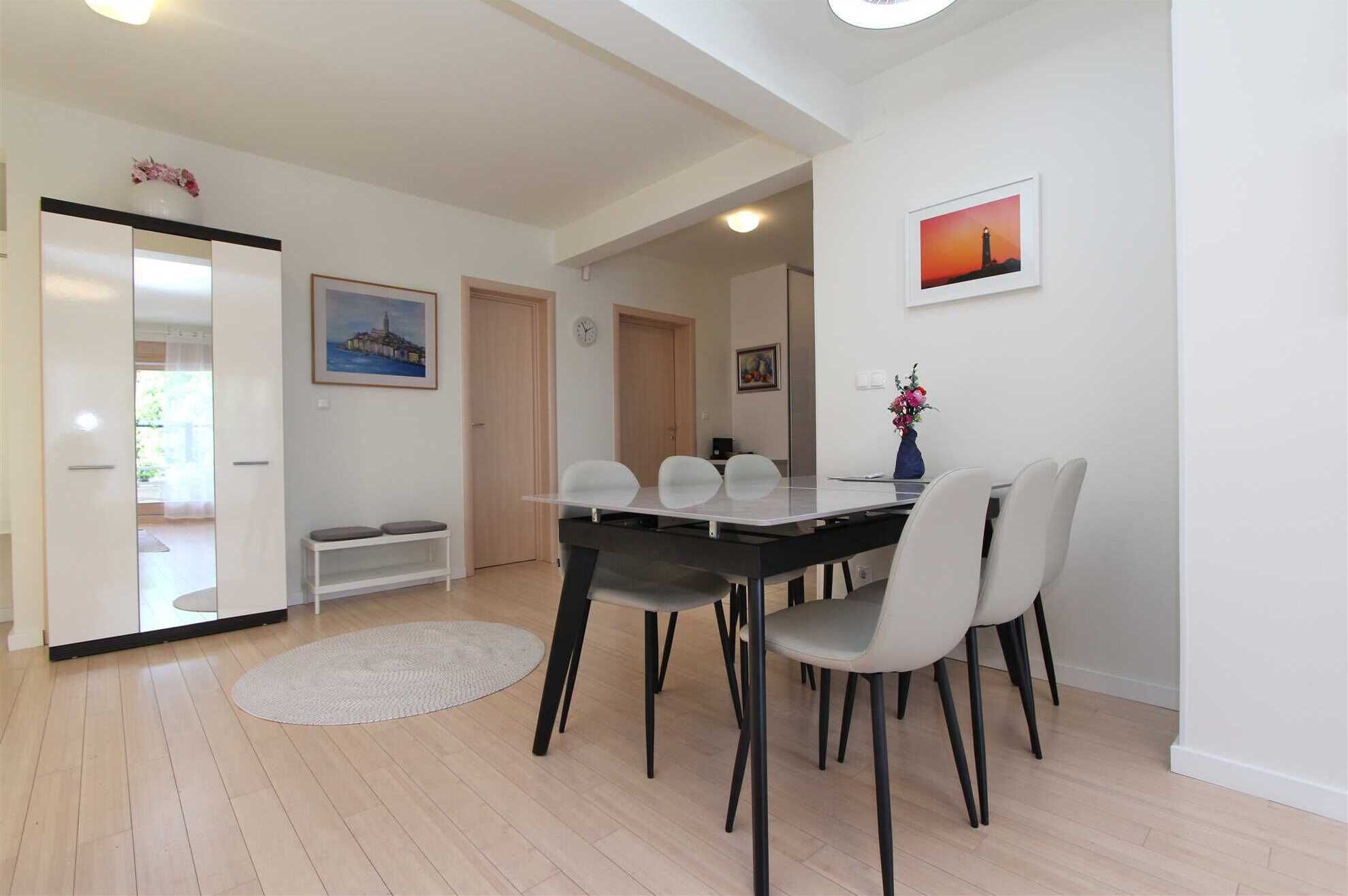 A modern dining area with a long table, six chairs, and a round rug.