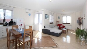 A modern living room with a sofa, a dining table with chairs, a kitchen area with a microwave, and a TV mounted on the wall. - DADO One-Bedroom Apartment (Putini)