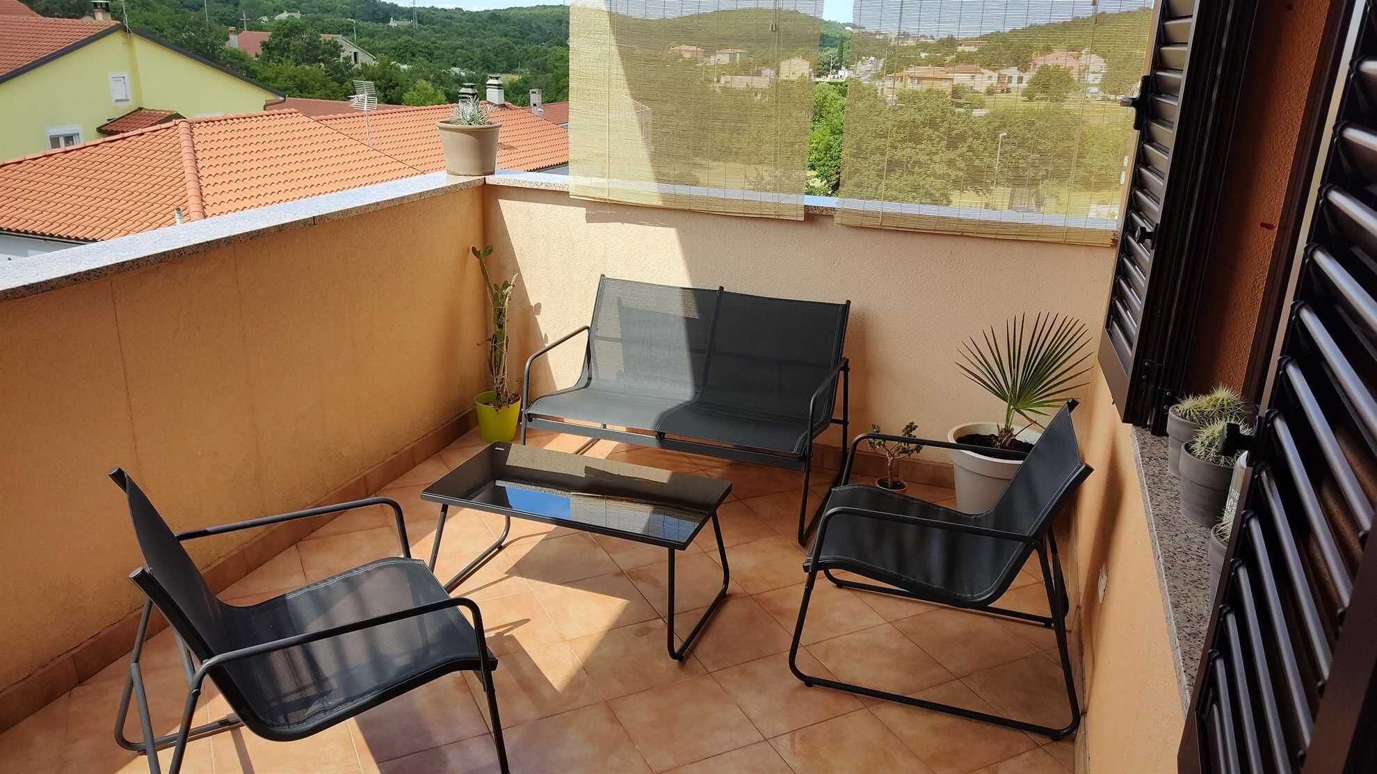 Een balkon met twee zwarte stoelen, een glazen tafel en potplanten.