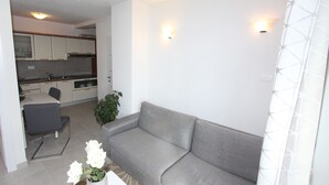 Ein modernes Wohnzimmer mit einem grauen Sofa, einem Esstisch und einer Küche im Hintergrund.