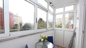 Ein Eckzimmer mit Glastisch und Stühlen, einem Blumentopf und Blick auf Gebäude durch große Fenster.