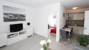 Ein modernes Wohnzimmer mit Flachbildfernseher, einem Essbereich mit Tisch und Stühlen sowie einer Küche mit Schränken und einem Kühlschrank.