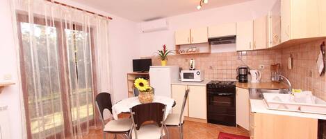 A compact kitchen with a dining area, featuring a microwave, stove, sink, and a small refrigerator.