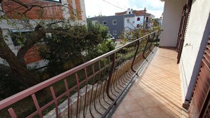 Ein Balkon mit Metallgeländer, gefliestem Boden und Blick auf benachbarte Gebäude und Bäume.