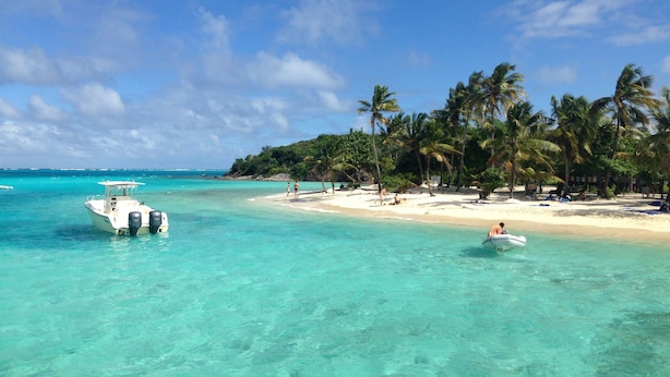 A beach with clear turquoise water, a boat, and palm trees. - Yacht Yota Bellavita (Gros Islet)