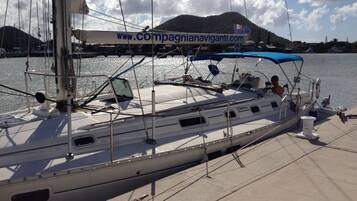 Un velero amarrado en un puerto deportivo, con un banner de sitio web, una persona en la cubierta y montañas al fondo.