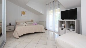 Ein Schlafzimmer mit Bett, Fernseher, Nachttisch, Heizkörper und einem Fenster mit Vorhängen.