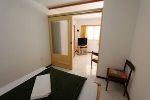 Ein Hotelzimmer mit einem Bett, einem Fernseher auf einem Schrank, einem Sessel und einer Tür zu einem anderen Raum.