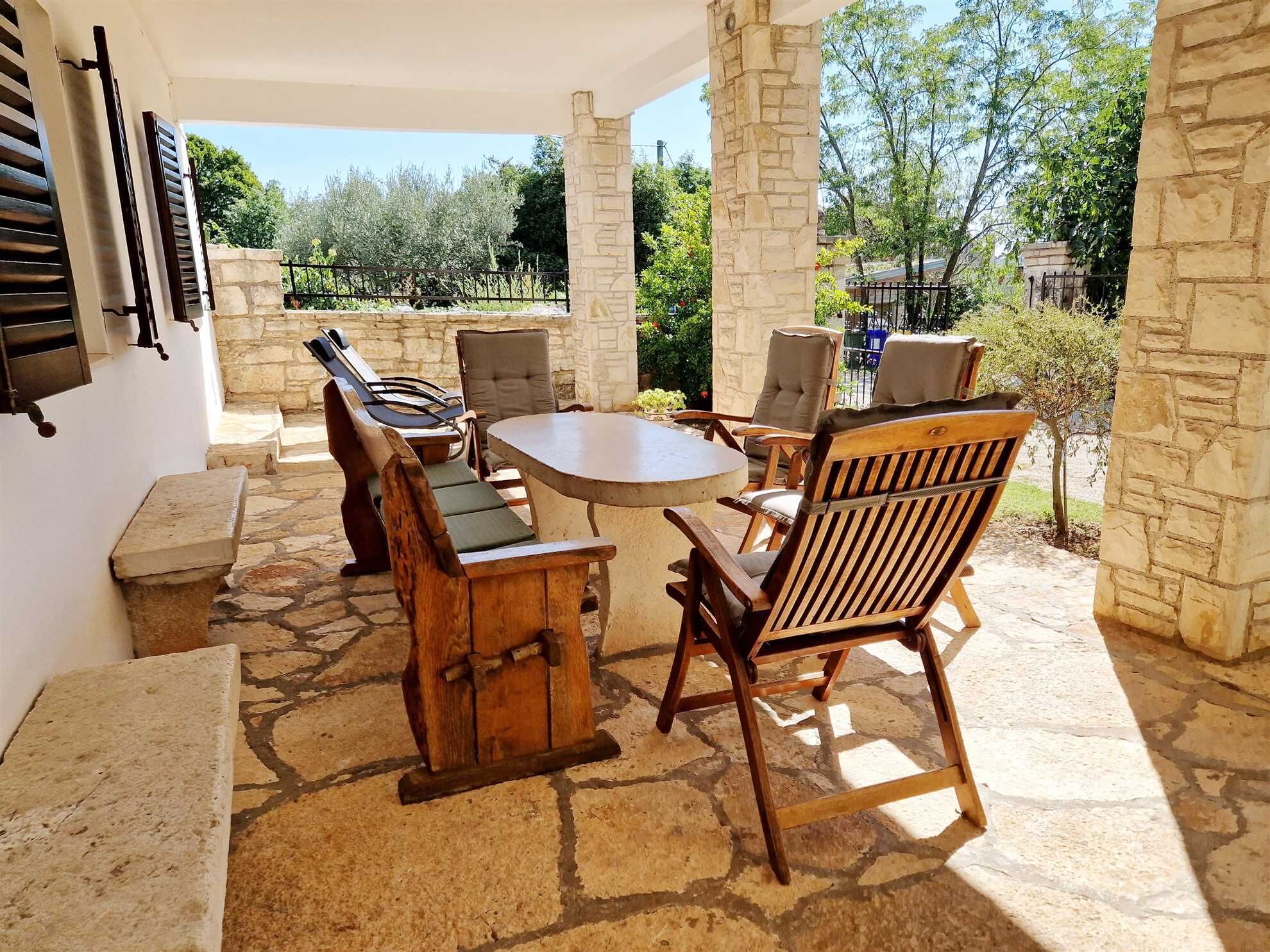 An outdoor patio with stone flooring, a round table, and wooden chairs.